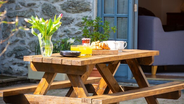 Un tavolo da picnic in legno con un bicchiere di succo d'arancia, croissant e un vaso di fiori.