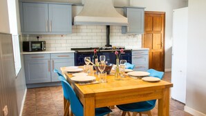 A modern kitchen with blue cabinets, a wooden dining table set with plates and glasses, and a built-in oven. - Cosy Luxury Cottage - Hot Tub - Private Estate (Rhosneigr)