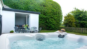 A hot tub with a table and chairs nearby, a small potted plant, and a wooden fence in the background. - Cosy Luxury Cottage - Hot Tub - Private Estate (Rhosneigr)