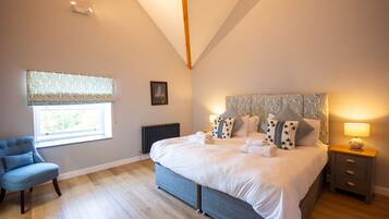 A bedroom with a bed, a chair, a bedside table, a lamp, a window with curtains, and a radiator.