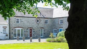 A stone building with a red door, multiple windows, and a gravel driveway. - Stylish Cottage - Hot Tub - Garden - Near Beach (Rhosneigr)