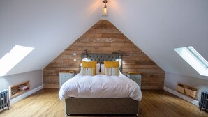 A bedroom with a sloped ceiling, a bed with a grey headboard, two bedside tables, and a skylight. - Rustic Couples Retreat - Hot Tub - Private Estate (Rhosneigr)