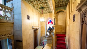 Un vaste hall d’entrée avec un plafond richement décoré, un escalier recouvert d’une moquette rouge et un vase ornemental.