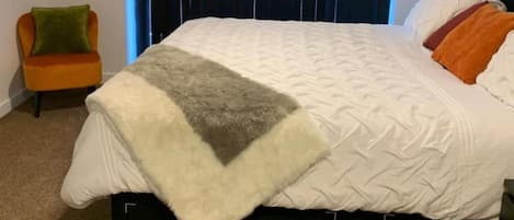 A bed with a white quilt and a gray throw blanket.