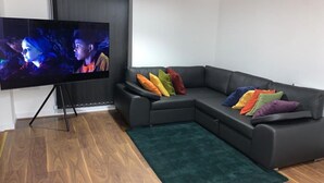 A modern living room with a sectional sofa, a flat-screen TV on a stand, and a green area rug. - Posh 1 Bed Flat-direct Links to Central London (Grays)