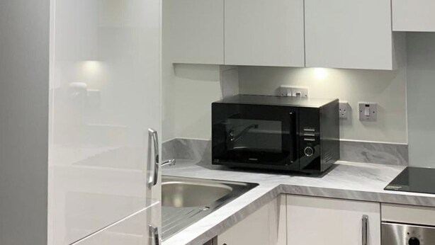 A modern kitchen with white cabinets, a black microwave, and stainless steel appliances. - Posh 1 Bed Flat-direct Links to Central London (Grays)