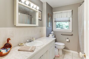 Une salle de bain avec un double lavabo, un grand miroir avec éclairage intégré, des toilettes et une fenêtre avec un rideau.