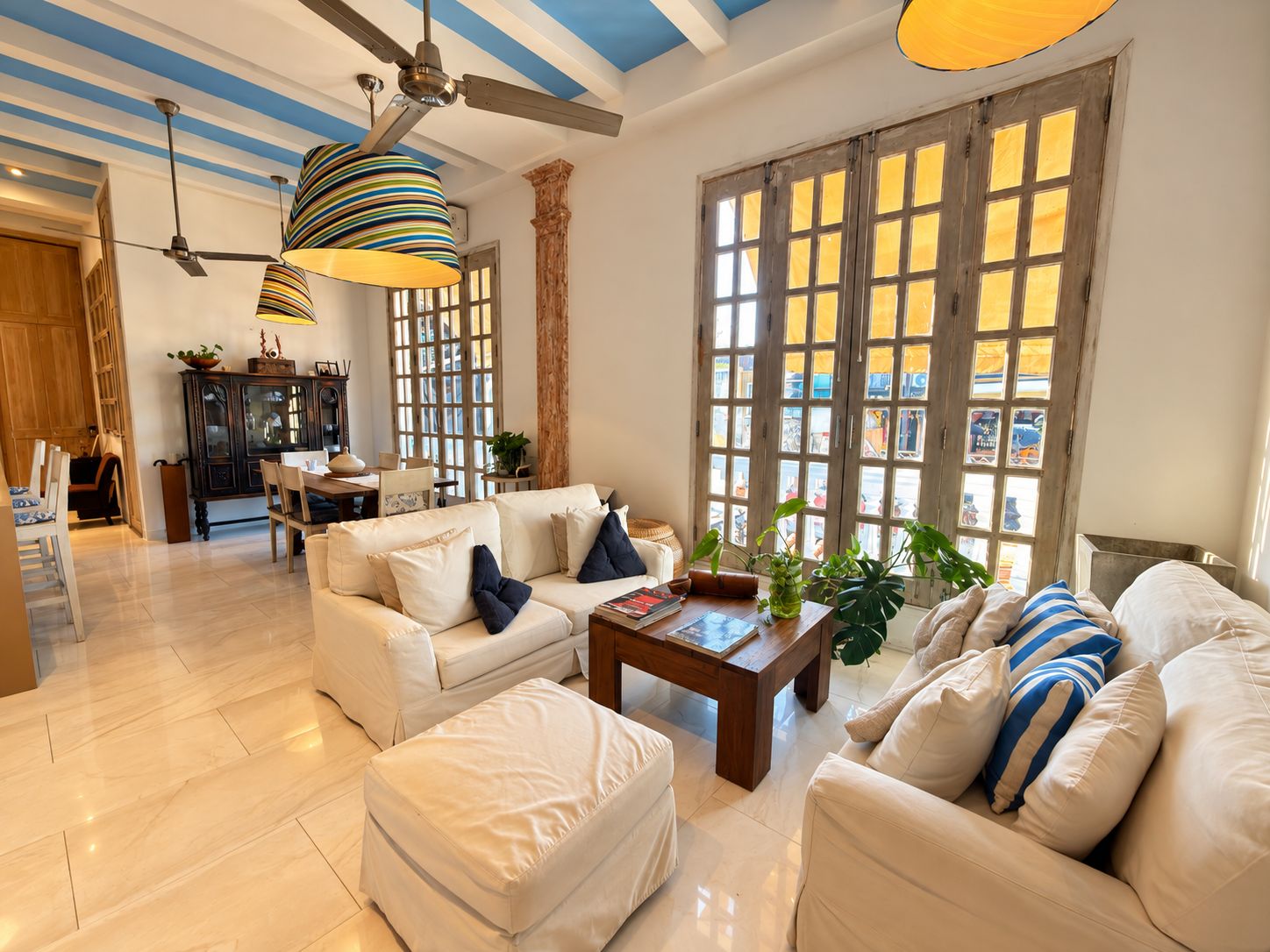 A spacious living room with a high ceiling, a dining area, and large windows with wooden frames.