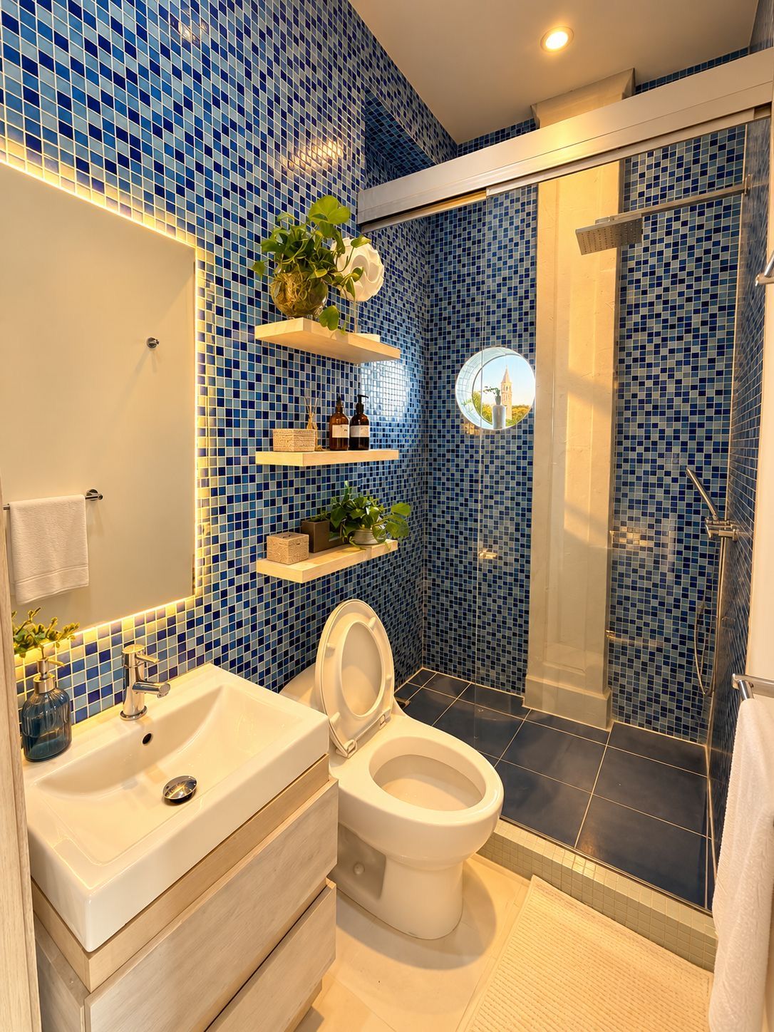 Baño con lavamanos, inodoro y ducha blancos. Hay estantes con plantas y artículos de aseo.
