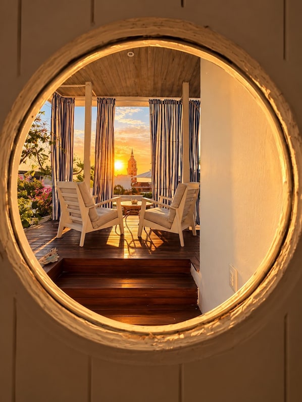 A circular window with a view of a wooden deck, two chairs, and a table. - Casa Lazuli 303 Cartagena (Cartagena)