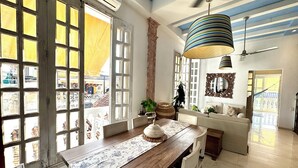 Un coin repas avec une table en bois, des chaises et un chemin de table à motifs. Une grande fenêtre à carreaux offre une vue sur l’extérieur.