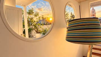 Un interior moderno con una escalera, un espejo redondo que refleja un atardecer y una lámpara a rayas.