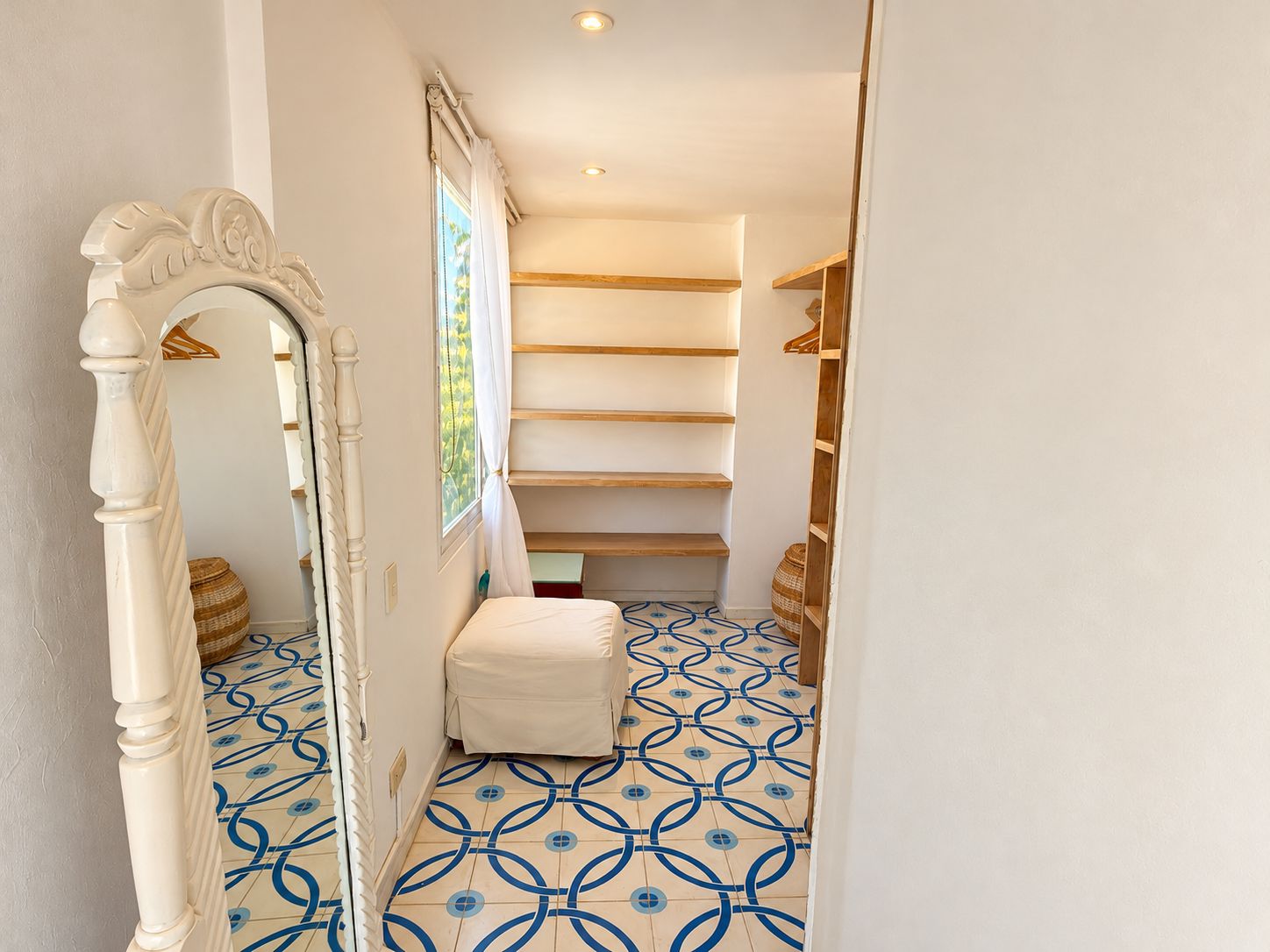 Un estrecho pasillo con piso estampado, una puerta blanca con picaporte decorativo y una escalera de madera que lleva a una plataforma.