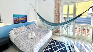 Une chambre avec un lit, un hamac, un tableau et une vue sur l’extérieur.