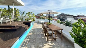 Une terrasse sur le toit, aménagée avec des meubles en bois, des plantes en pot et offrant une vue sur le paysage urbain.