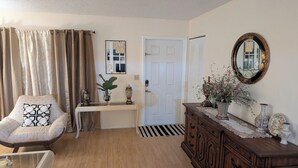 A living room with a beige armchair, a small table with decorative items, a wooden dresser, and a mirror on the wall. - Family-friendly•Quiet•Near Beaches, Parks & Cities (Palm Bay)