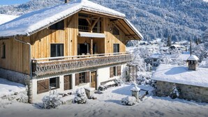 Un chalet en bois doté d’un balcon, entouré de montagnes et d’arbres couverts de neige.