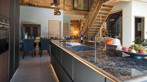 A modern kitchen with a central island, wooden ceiling beams, and a staircase leading to an upper level.