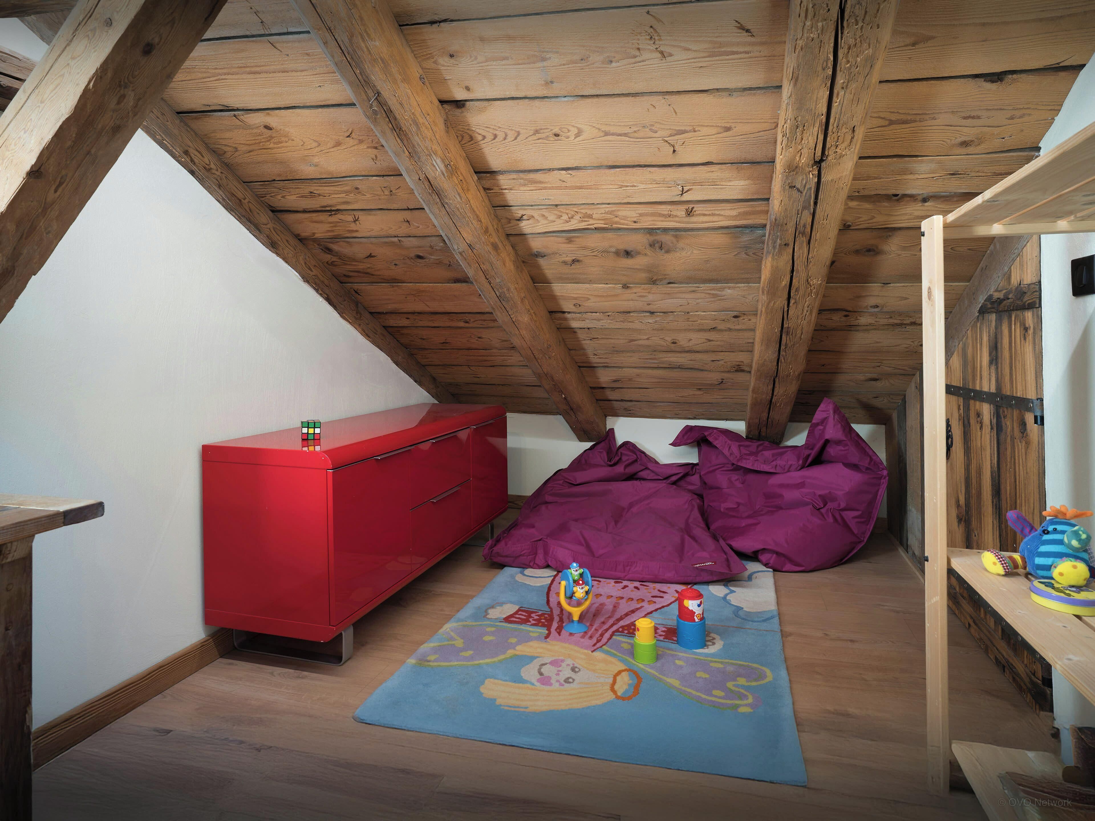A room with a sloped ceiling, a red dresser, a colorful play mat, and toys on the floor.