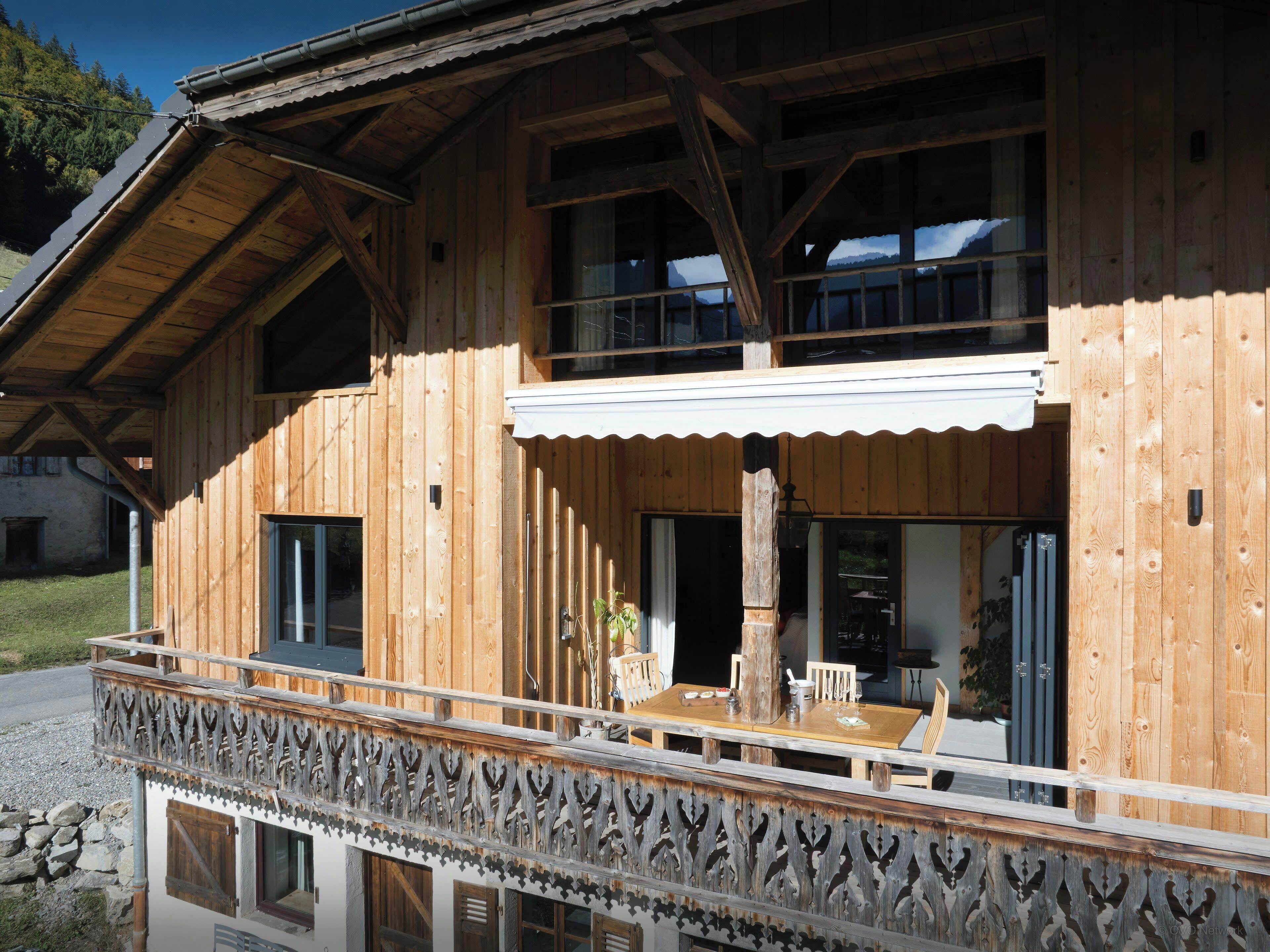 A wooden chalet with a balcony, large windows, and a dining area.