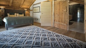 A bedroom with a wooden ceiling, a bed with a patterned rug, and a sliding door leading to a bathroom.