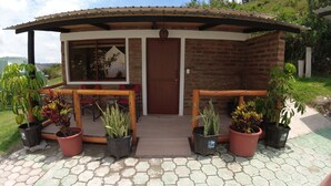 A small brick building with a wooden porch, potted plants, and a view of the surrounding landscape.