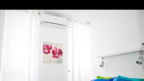 A bedroom with a bed, white curtains, a wall-mounted air conditioning unit, and a painting of flowers. - Cozy Trastevere Apartment - Great Location, Fast Wi-Fi & A/C (Roma)