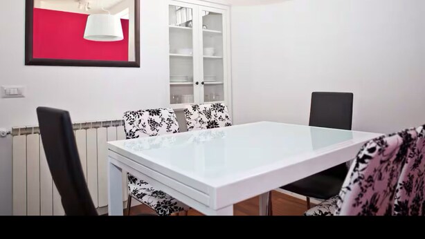 A dining area with a white table, black and white patterned chairs, a white cabinet, and a red wall. - Cozy Trastevere Apartment - Great Location, Fast Wi-Fi & A/C (Roma)