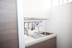 A modern kitchen with a stainless steel sink, white cabinets, and a utensil holder.