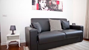 Una sala moderna con un sofá de cuero negro, un cojín decorativo estampado, una pequeña mesita auxiliar con una lámpara y un cuadro abstracto grande en la pared.