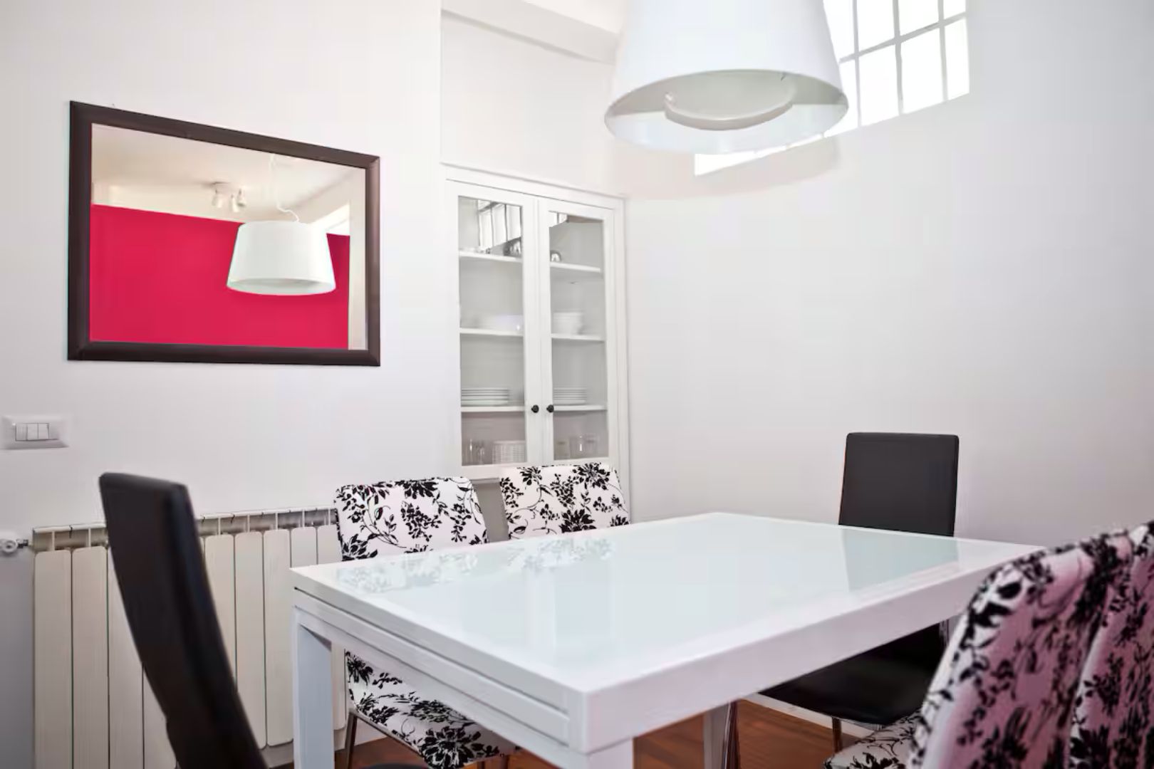 Un coin repas avec une table blanche, des chaises à motifs noirs et blancs, un meuble blanc et un mur rouge.