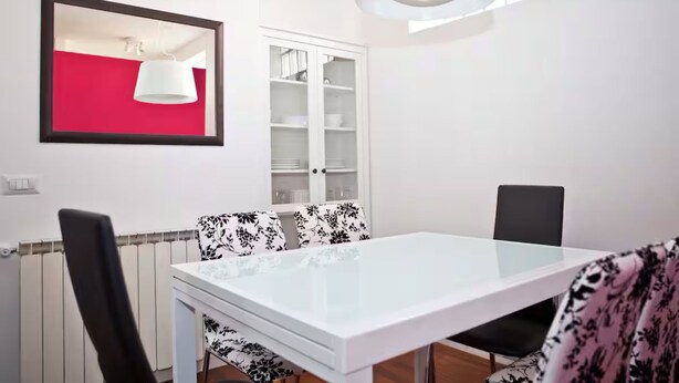 Un comedor con una mesa blanca, sillas a cuadros blanco y negro, un armario blanco y una pared roja.