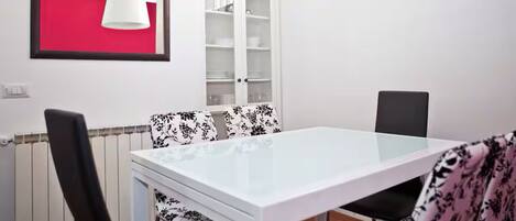 Un coin repas avec une table blanche, des chaises à motifs noirs et blancs, un meuble blanc et un mur rouge.