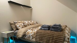 Un letto rifatto con cura, lenzuola a motivi floreali, un comodino con una lampada e un pavimento illuminato di blu.