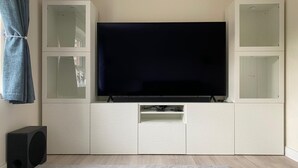 Un soggiorno moderno con una TV a schermo piatto montata su un mobile bianco, un tappeto grigio grande e un altoparlante sul pavimento.