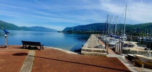 Ein Yachthafen mit vertäuten Booten, einer Bank und freiem Blick auf das Wasser und die entfernten Berge.