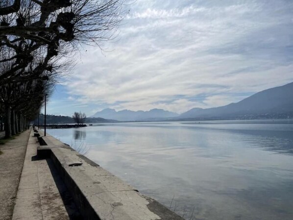 A calm lake with a concrete walkway and leafless trees on one side.