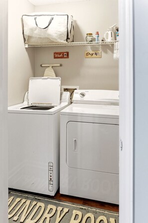 Een wasruimte met een wasmachine, droger en een plank met schoonmaakmiddelen.