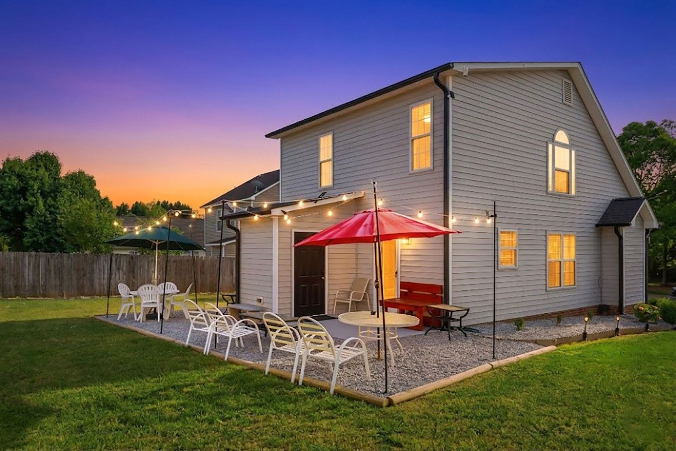 Una casa de dos pisos con un patio, mobiliario exterior y luces colgantes.