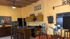 Una cucina compatta con mobili in legno e un'isola centrale, un'area pranzo con tovaglia colorata e una ventola a soffitto.