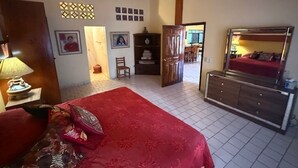Una camera da letto con un letto grande, un'armadio in legno, una scrivania con una lampada e una porta che dà su un'altra stanza.