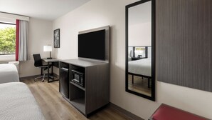 Une chambre d’hôtel avec un lit, un bureau avec une télévision, un miroir et un banc rouge.