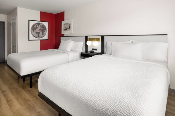 Ein Hotelzimmer mit zwei Einzelbetten, einem Nachttisch mit Lampe und einer roten Akzentwand.