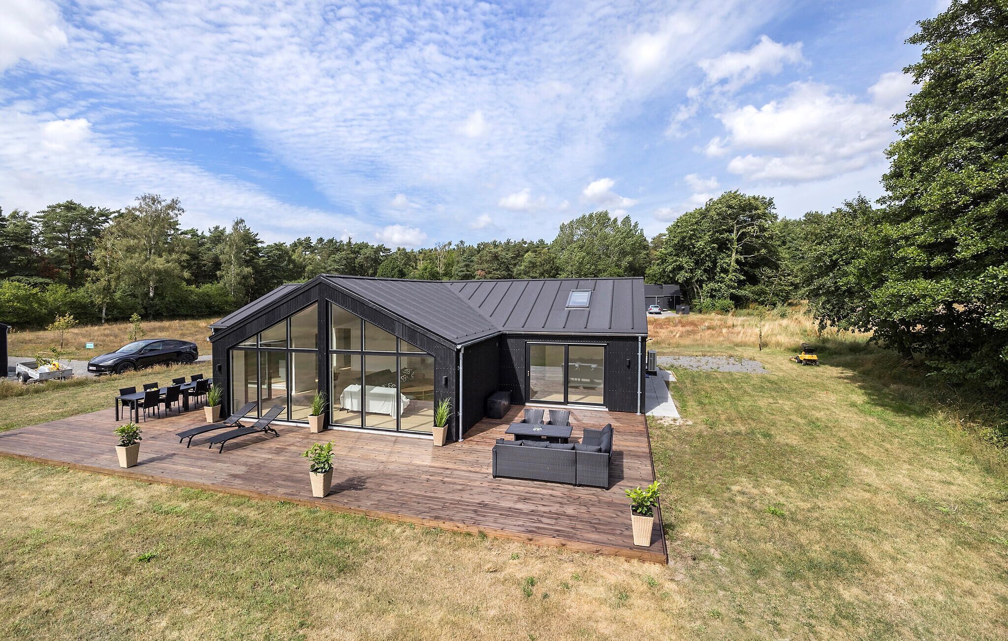 A modern house with a large glass facade, a deck with outdoor furniture, and a surrounding grassy area.