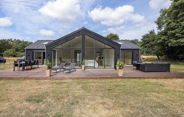 Ein modernes Haus mit einer großen Glasfassade, einer Terrasse mit Gartenmöbeln und einem Rasen.