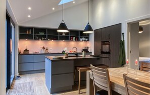 Eine moderne Küche mit einer zentralen Kochinsel, Pendelleuchten und einem Essbereich mit Holztisch und -stühlen.