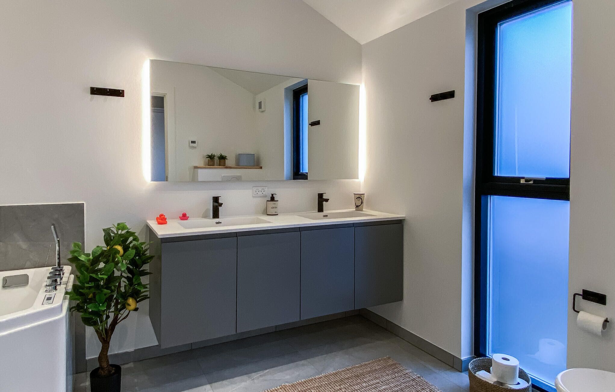 A modern bathroom with two sinks, a large mirror, and a window.