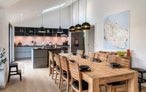 Cozinha moderna com ilha central, mesa de jantar de madeira e cadeiras. Há luminárias pendentes sobre a ilha e um mapa grande na parede.