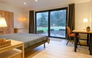 Ein modernes Schlafzimmer mit Bett, Schreibtisch und Blick auf einen Garten durch eine Schiebetür.