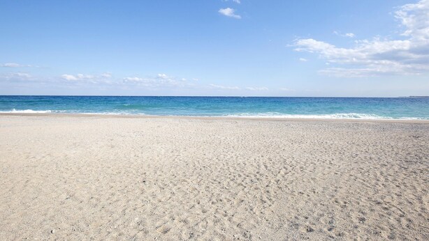 Une vaste plage de sable fin, avec des vagues douces et un ciel bleu dégagé.